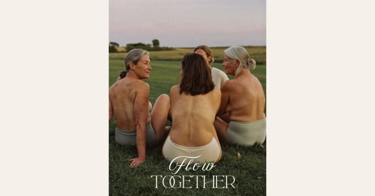 Four women of different ages sit in a circle on the grass at dusk, talking easily together. Seen from behind, in plain cotton underwear, with the Flow Together wordmark beneath. AI-generated image.